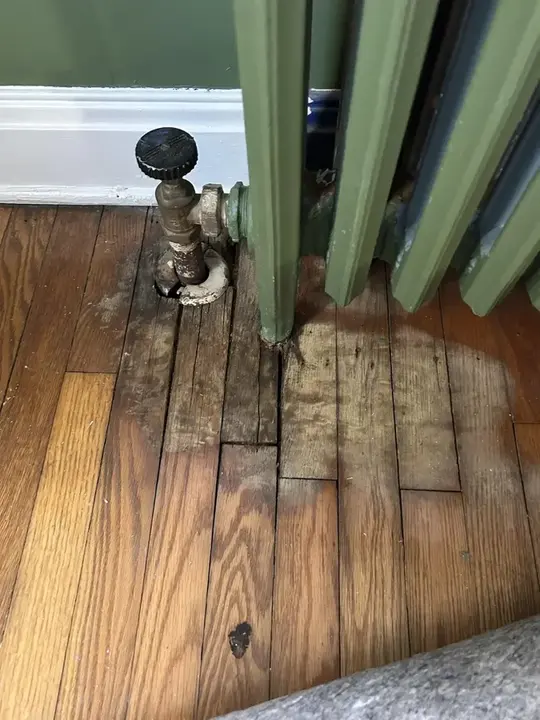 Darkened oak floor boards under a leaking steam radiator valve