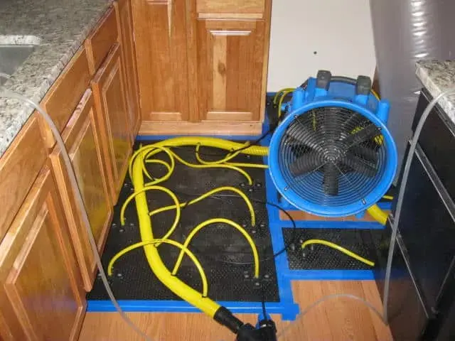 Drying mats and an air mover drying hardwood under kitchen cabinets after a dishwasher leak