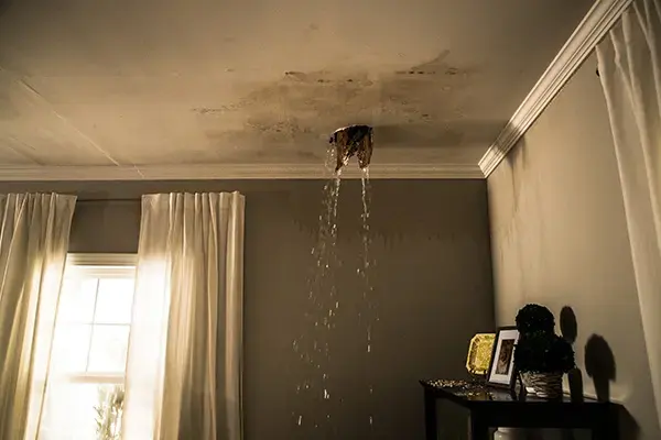Water pouring through a ceiling light opening into a room below