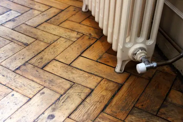 Water-stained herringbone hardwood under a leaking cast-iron radiator valve